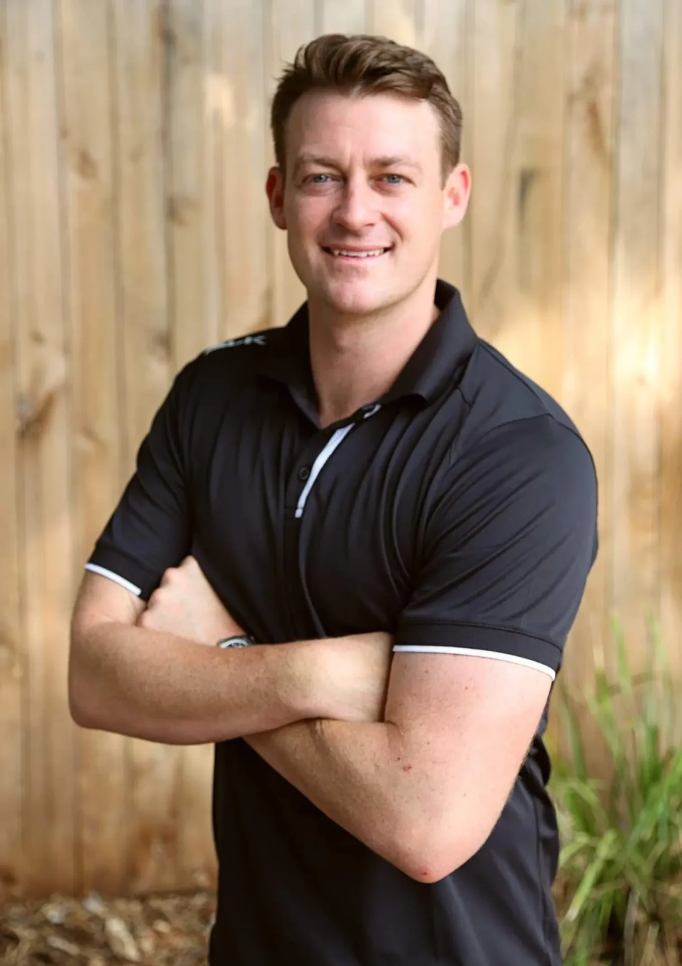 Man smiling with arms crossed, wooden background.
